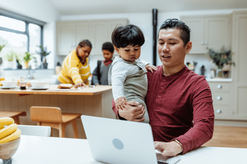 Entrepreneur father working from home on laptop and holding baby