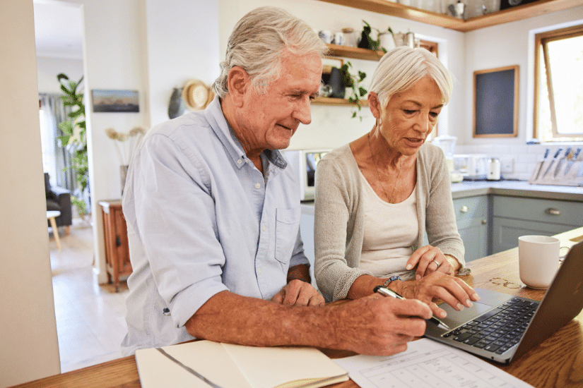 Senior couple going over their home finances together using a laptop while sitting at a table in their kitchen at home.